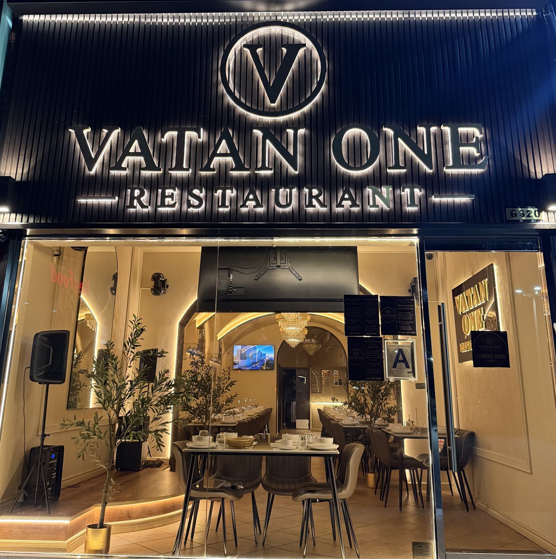 Vatan One Restaurant facade at night, backlit brass sign over a warm-lit dining room